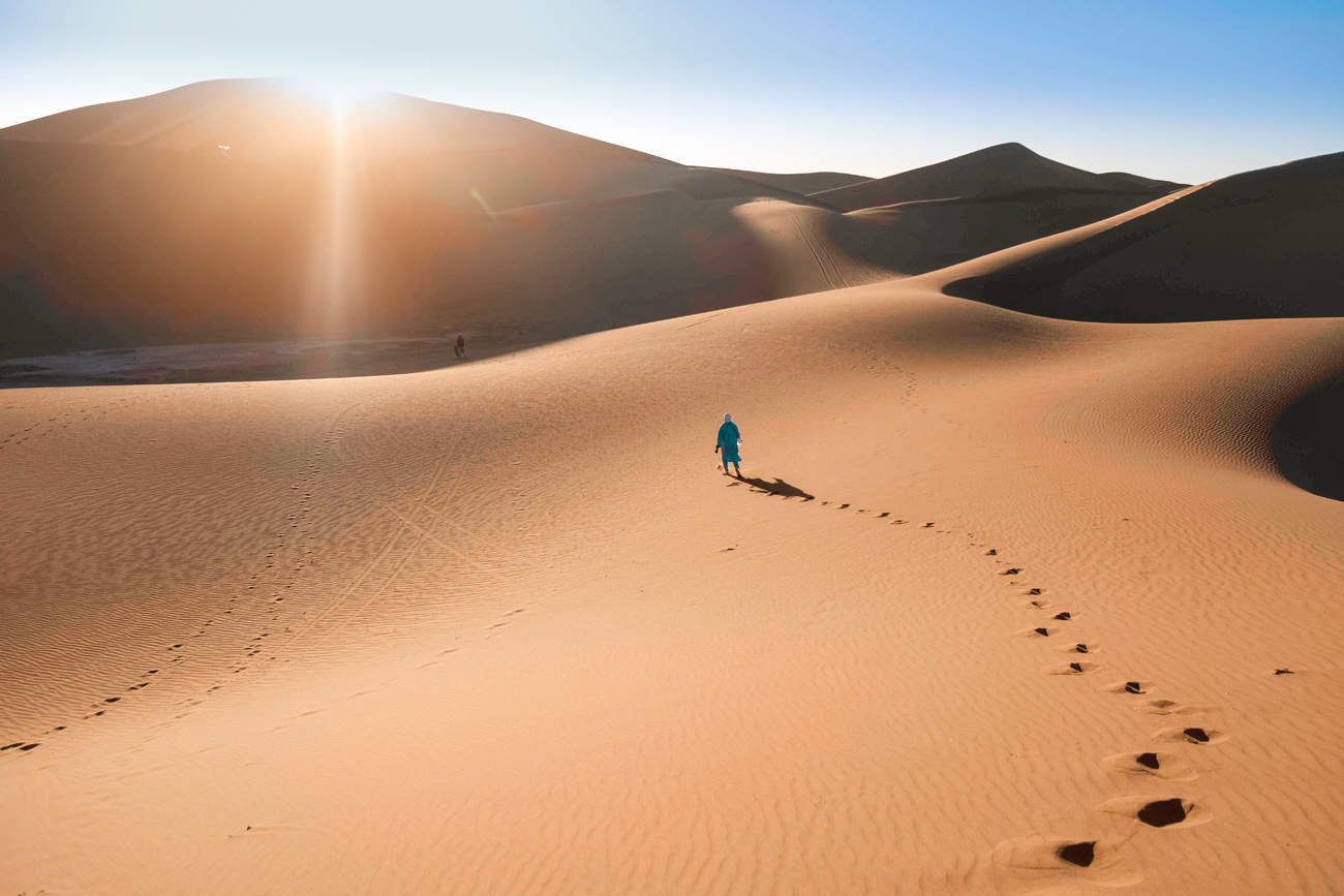 A lone walker leaving footprints across the Sahara dunes, far from phone signal